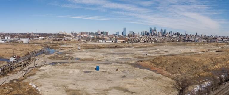 The former refinery is visible in the distance, with a bare, dirt field in the foreground.