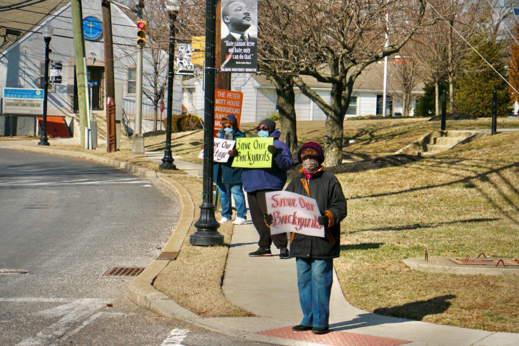Lawnside residents stand along Warwick Road holding up protest signs
