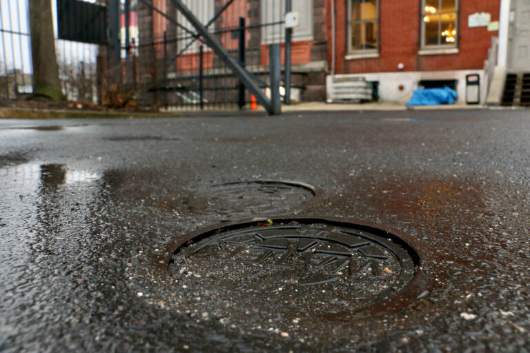 Metal caps marked ''WATER'' are the only evidence of the 400-foot wells beneath the parking lot of the German Society of Pennsylvania on Spring Garden Street. The wells tap the geothermal energy of the earth to heat and cool the society's building. (Emma Lee/WHYY)