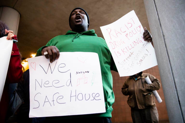 A protester holds signs in support of a supervised injection site