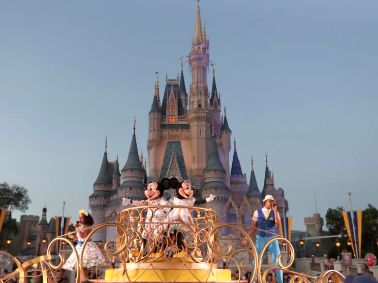 FILE - Mickey and Minnie Mouse perform during a parade as they pass by the Cinderella Castle at the Magic Kingdom theme park at Walt Disney World in Lake Buena Vista, Fla. The theme park resort announced Tuesday, Feb. 15, 2022, that face coverings will be optional for fully-vaccinated visitors in all indoor and outdoor locations, with one exception. Face masks still will be needed for visitors ages 2 and older on enclosed transportation, such as the resort's monorail, buses and the resort's sky gondola