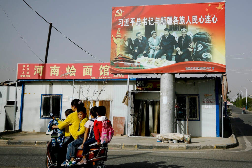 A Uyghur woman rides past a billboard showing China's president