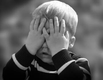 A child covers his face with his hands.