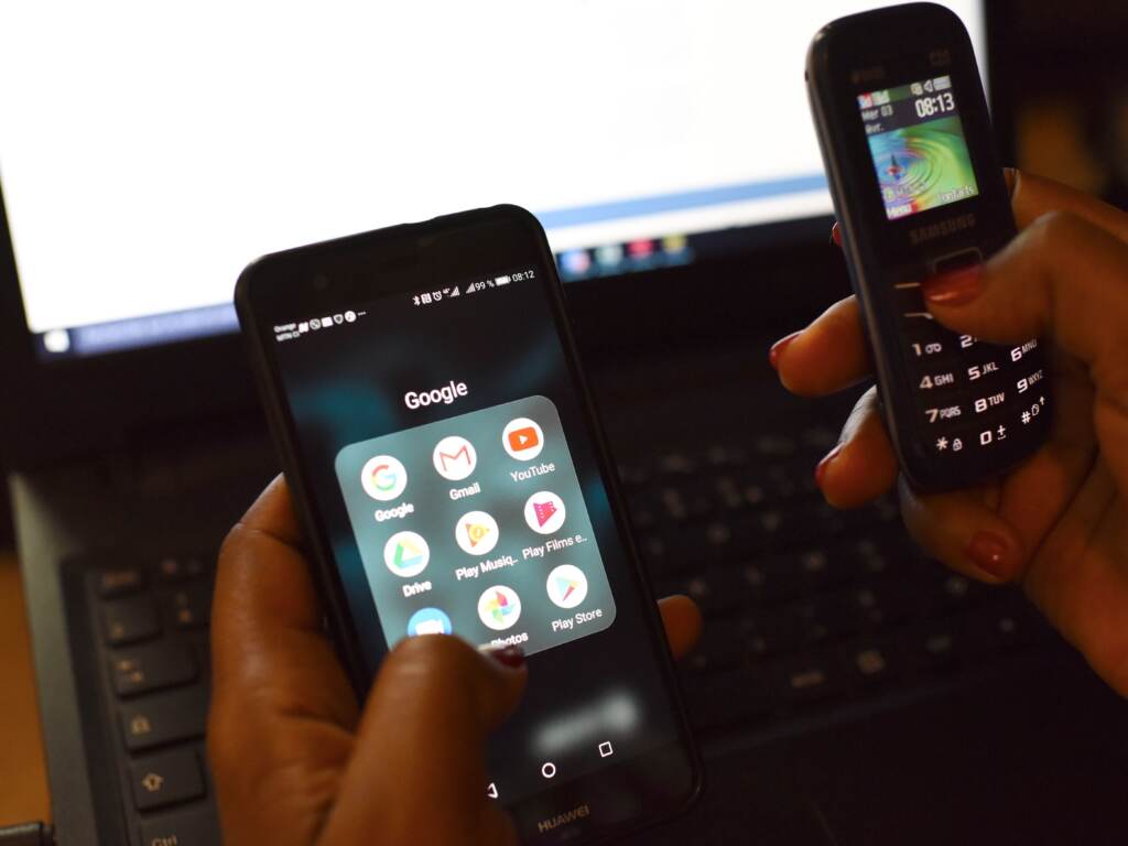 A woman uses a smartphone and a mobilephone in front of a laptop 