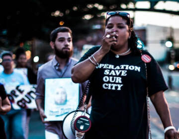 Rosalind Pichardo leading a crowd of people with a megaphone, wearing an 