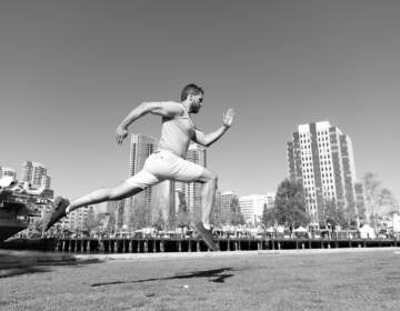 A black and white image of a man leaping and running with a city skyline in the background