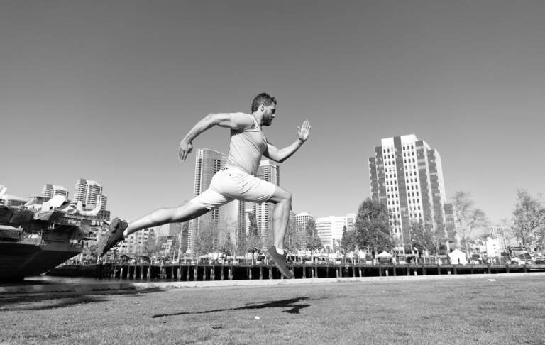 A black and white image of a man leaping and running with a city skyline in the background