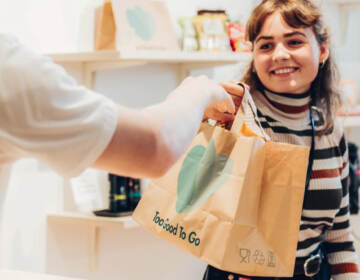 A young woman being handed food in a Too Good To Go bag