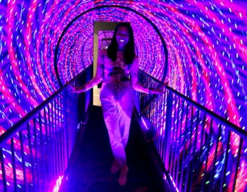 Stacy Rangel Stec walks through a tunnel whose swirling lights create an illusion of motion at the Museum of Illusions in Philadelphia. (Emma Lee/WHYY)