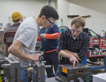 Mitch Engleka, 28, manufacturing engineer (right) and Nick Ball, a manufacturing technician (left), inspect a mold that creates latches to secure the spare tire on a Dodge Durango at Southco in Concordville, Pa.(Kimberly Paynter/WHYY)