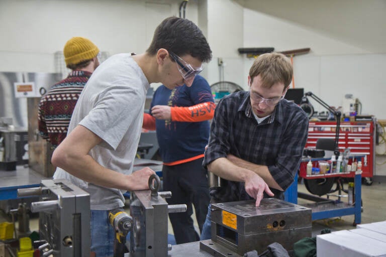 Mitch Engleka, 28, manufacturing engineer (right) and Nick Ball, a manufacturing technician (left), inspect a mold that creates latches to secure the spare tire on a Dodge Durango at Southco in Concordville, Pa.(Kimberly Paynter/WHYY)