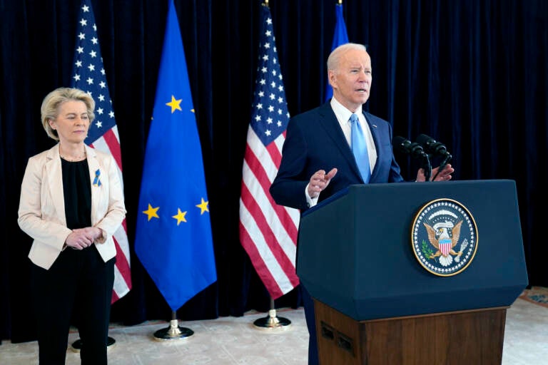 President Joe Biden speaks at a podium, with European Commission President Ursula von der Leyen standing in the background.