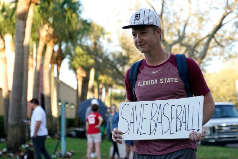 Baseball fan Noah McMurrain of Boynton Beach, Fla., stands outside Roger Dean Stadium as Major League Baseball negotiations continue in an attempt to reach an agreement to salvage a March 31 start to the regular season, Monday, Feb. 28, 2022, in Jupiter, Fla. (AP Photo/Lynne Sladky)