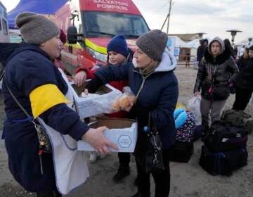 A Moldovan volunteer distributes food to refugees who are leaving to Romania after fleeing from Ukraine, at the border crossing in Palanca, Moldova, Thursday, March 17, 2022