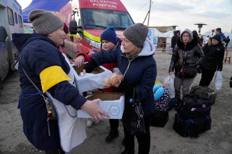 A Moldovan volunteer distributes food to refugees who are leaving to Romania after fleeing from Ukraine, at the border crossing in Palanca, Moldova, Thursday, March 17, 2022