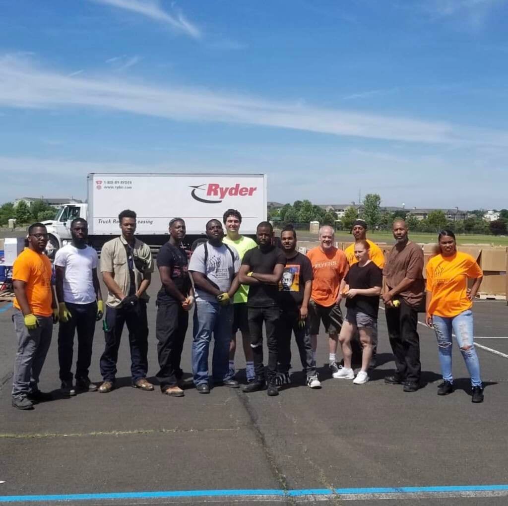 A group of people stand smiling in a parking lot with a truck in the background.