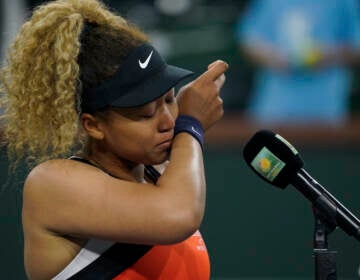 Tennis star Naomi Osaka appears to wipe tears from her face as she stands in front of a microphone.