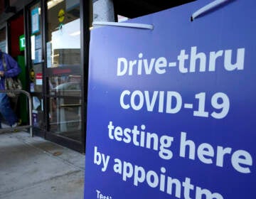 A passer-by walks past a sign that calls attention to COVID-19 testing while departing a Walgreens pharmacy