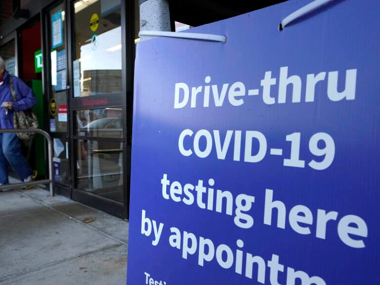 A passer-by walks past a sign that calls attention to COVID-19 testing while departing a Walgreens pharmacy