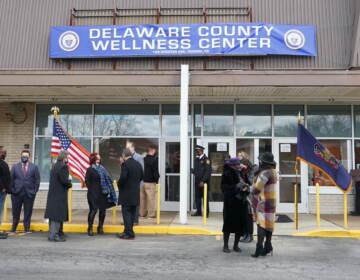 People stand outside of a building with a banner that reads, 