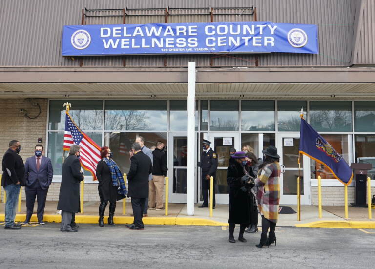 People stand outside of a building with a banner that reads, 