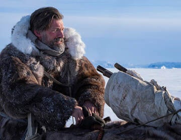 Nikolaj Costner-Waldau dressed in fur winter coats outside in Greenland on a sled