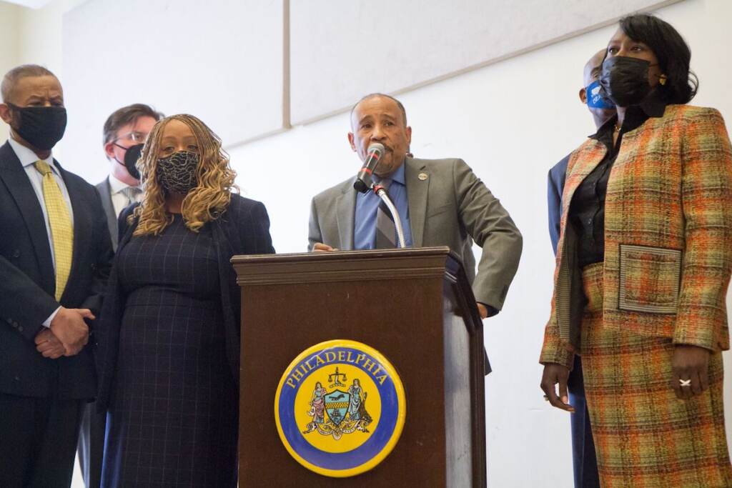 George Mosee, executive director of PAAN, speaks at the podium surrounded by elected officials and other stakeholders.