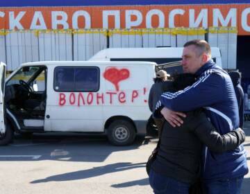 Olga and Oleksandr hug as they wait beside a vehicle painted with the word 