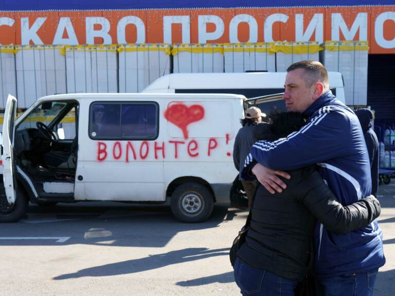 Olga and Oleksandr hug as they wait beside a vehicle painted with the word 