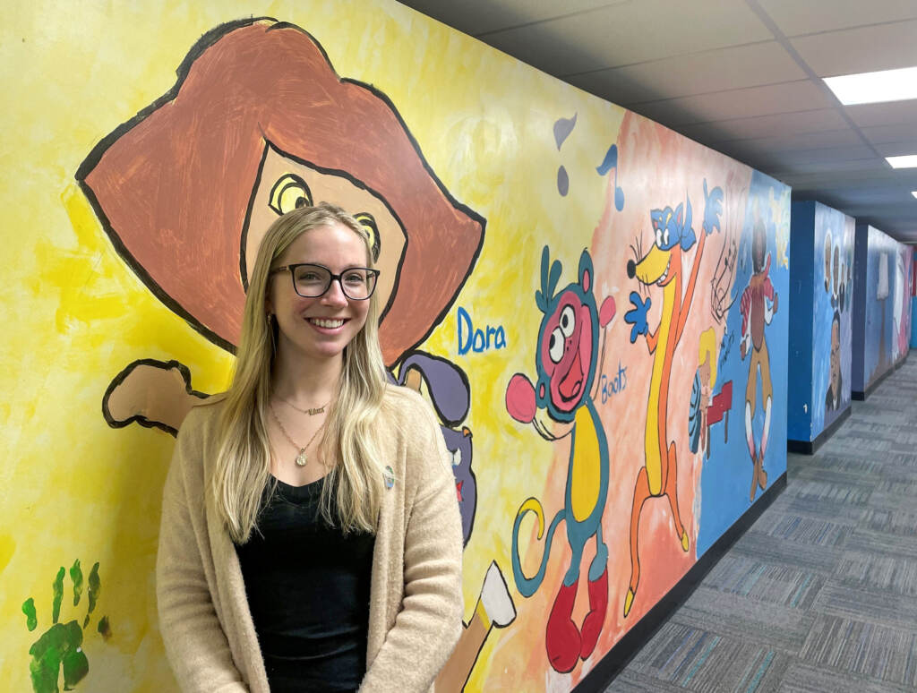 Katie Hitchens stands in front of a mural