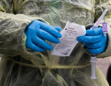 A close-up of a health care worker's hands, in blue gloves, handling an infusion for a patient at a drive-thru monoclonal antibody treatment.