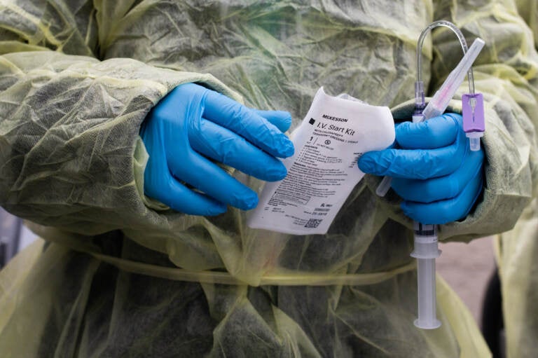 A close-up of a health care worker's hands, in blue gloves, handling an infusion for a patient at a drive-thru monoclonal antibody treatment.