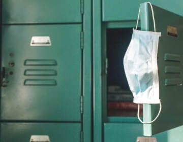 A surgical mask hangs from the open door of a green locker.