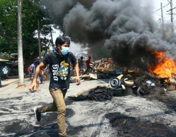 Anti-coup protesters run around a burning, makeshift barricade