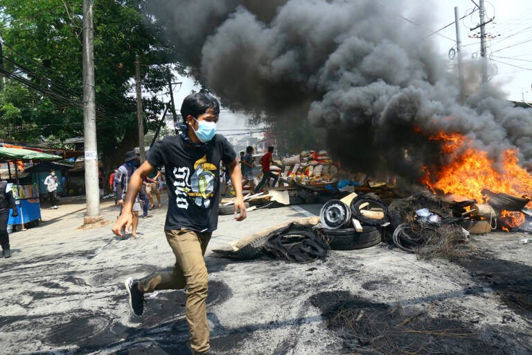 Anti-coup protesters run around a burning, makeshift barricade