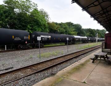 A black freight train, operated by Norfolk Souther, speeds by on a track, as seen from the former train station in Phoenixville, PA.