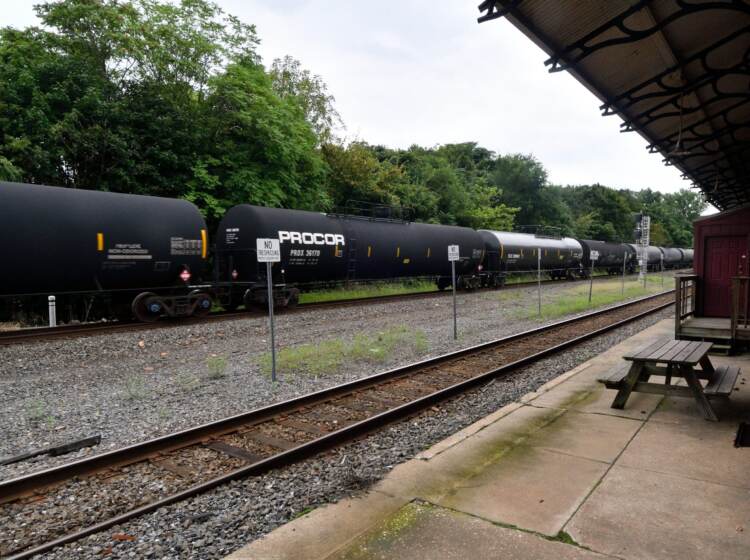 A black freight train, operated by Norfolk Souther, speeds by on a track, as seen from the former train station in Phoenixville, PA.