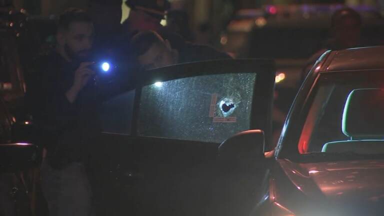 A police officer shines a flashlight onto a car window with a bullet hole in it