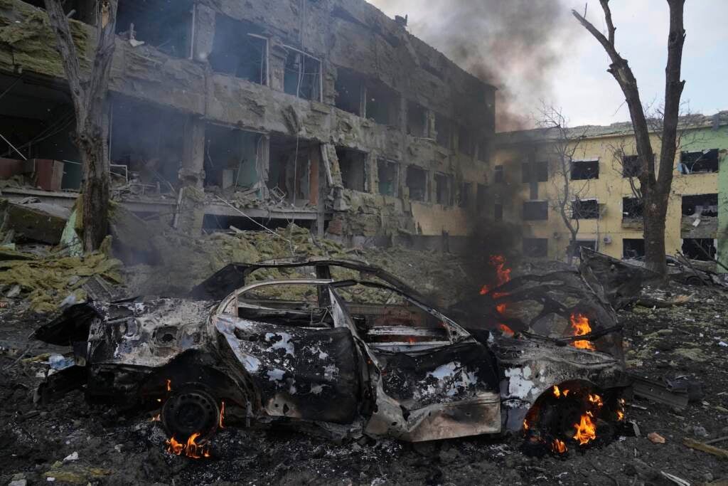 A car burns at the side of the damaged by shelling maternity hospital