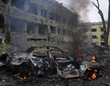 A car burns at the side of the damaged by shelling maternity hospital