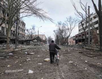 A man walks with a bicycle in a street damaged by shelling in Mariupol