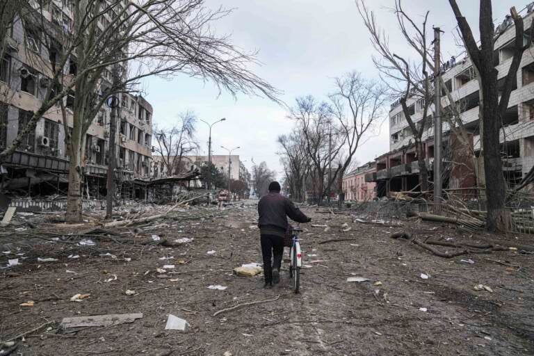 A man walks with a bicycle in a street damaged by shelling in Mariupol