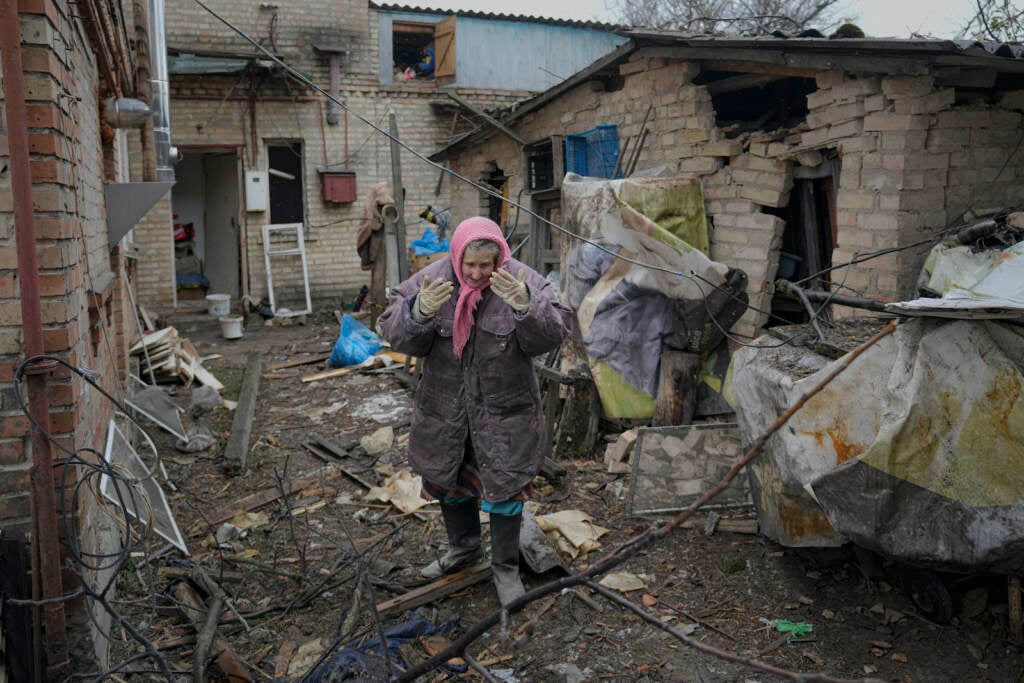 A woman is overwhelmed by emotion in the backyard of a house damaged by a Russian airstrike