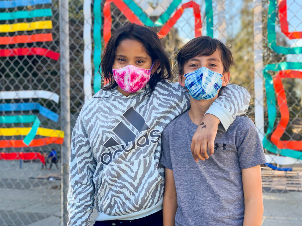 Two children pose for the camera. Both are wearing face masks.