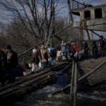 Ukrainians cross an improvised path under a destroyed bridge while fleeing Irpin