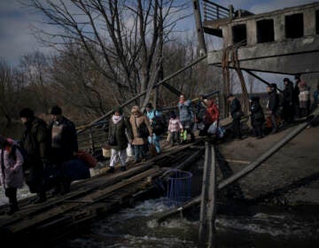 Ukrainians cross an improvised path under a destroyed bridge while fleeing Irpin