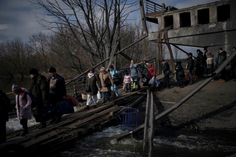 Ukrainians cross an improvised path under a destroyed bridge while fleeing Irpin