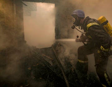 A Ukrainian firefighter sprays water inside a house destroyed by bombing in Kyiv