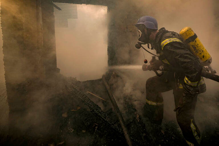 A Ukrainian firefighter sprays water inside a house destroyed by bombing in Kyiv