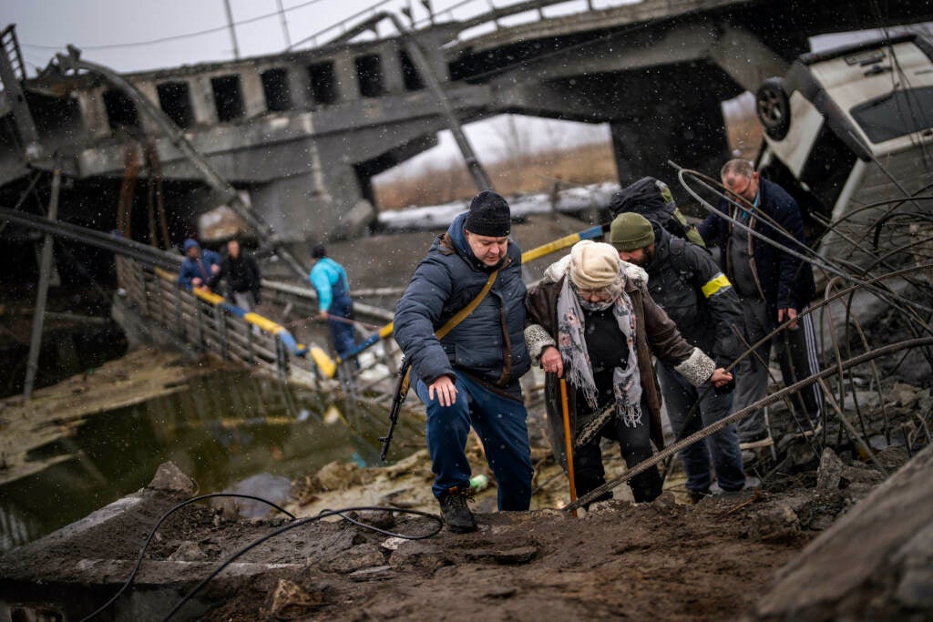 Local militiamen help a woman crossing a bridge destroyed by artillery